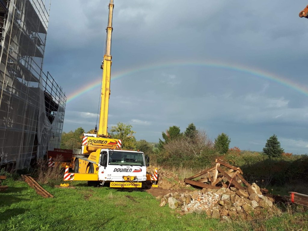Grue de chantier devant l'église Saint Paul de Reilhac en travaux de rénovation, avec un arc-en-ciel dans le ciel