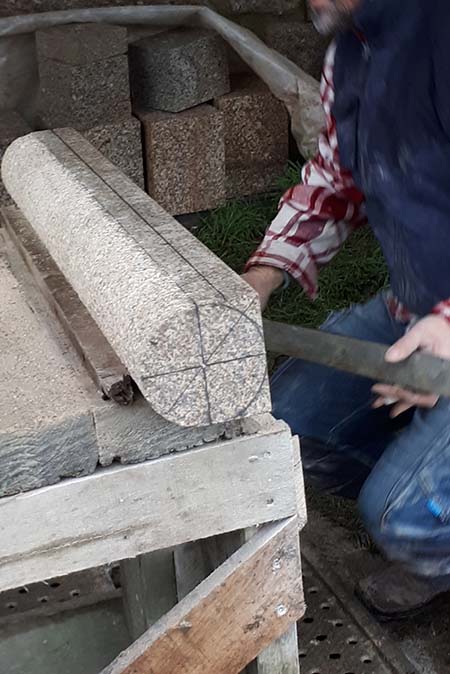 Un tailleur de pierre façonne un bloc de granit pour la restauration de l'église Saint Paul de Reilhac
